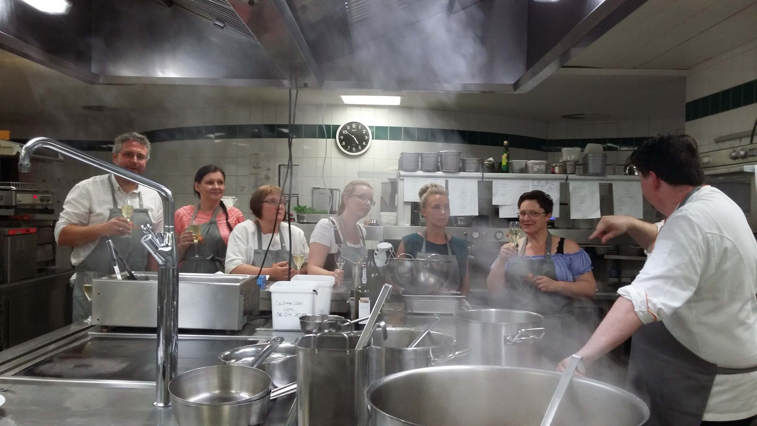 Frauen und Männer in einer Gastronomie-Küche beim Kochkurs zeigen Teamerlebnis Pflegefachkraft bei VitaConSana
